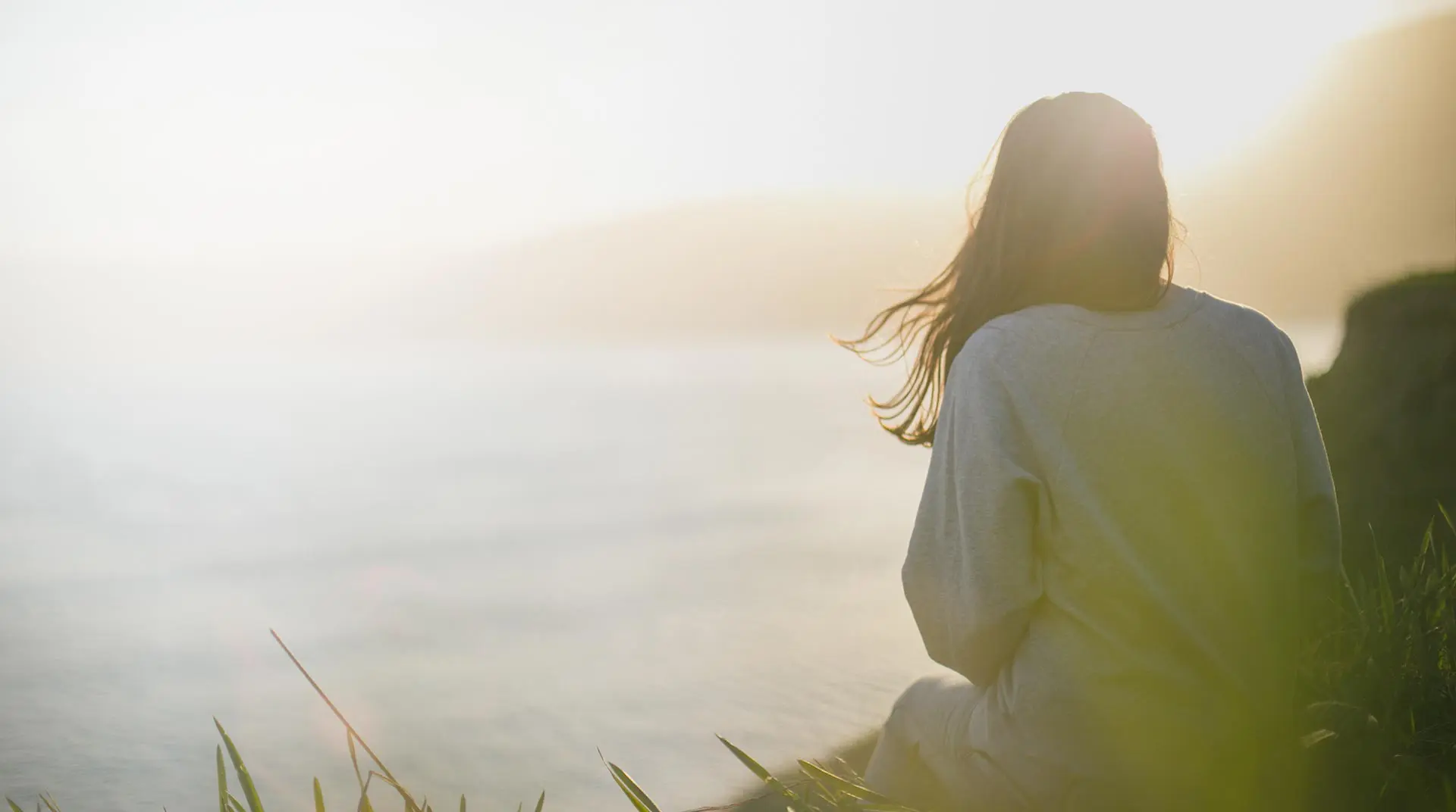 A woman sitting on the beach looking out at the ocean.